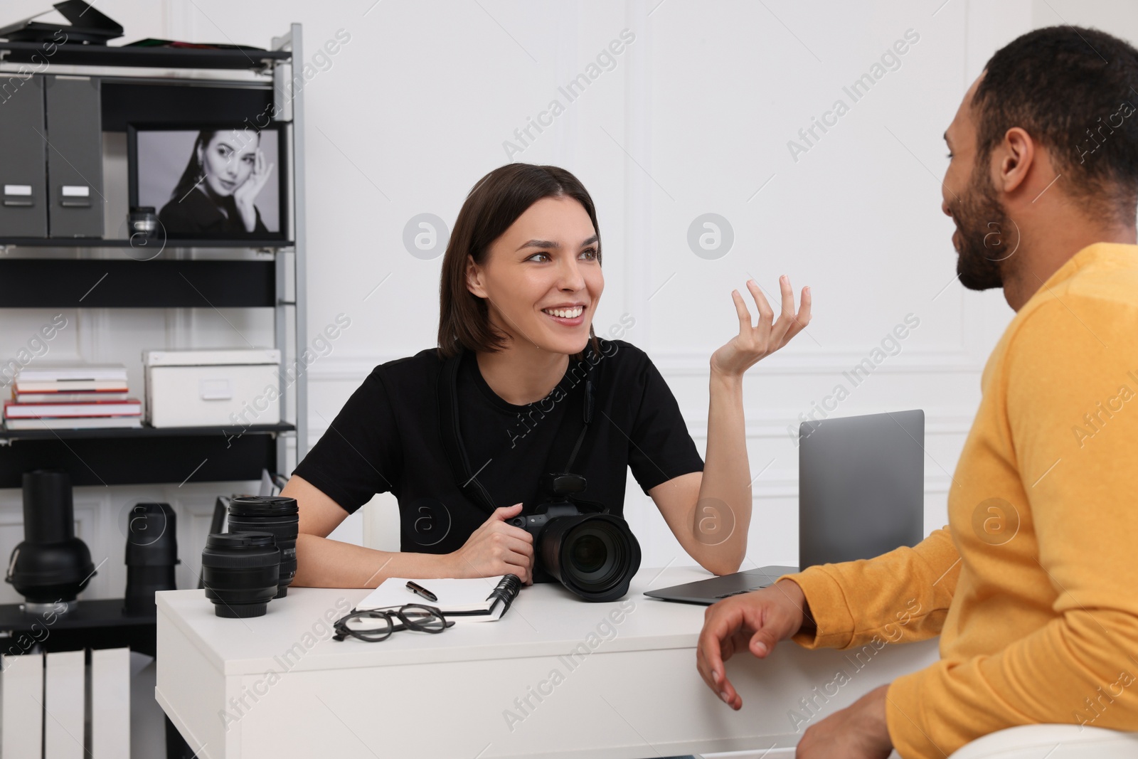 Photo of Young professional photographer holding camera while talking with man in modern photo studio