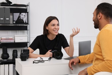 Young professional photographer holding camera while talking with man in modern photo studio