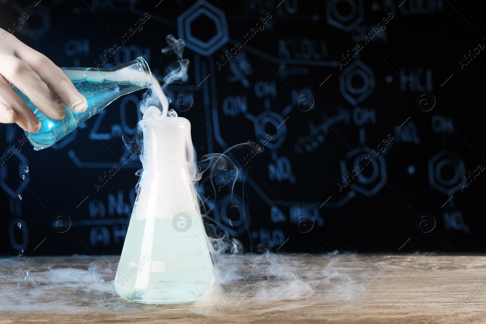 Photo of Scientist working with laboratory glassware and space for text at wooden table, closeup. Chemical reaction