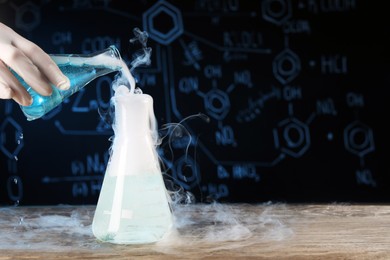 Photo of Scientist working with laboratory glassware and space for text at wooden table, closeup. Chemical reaction