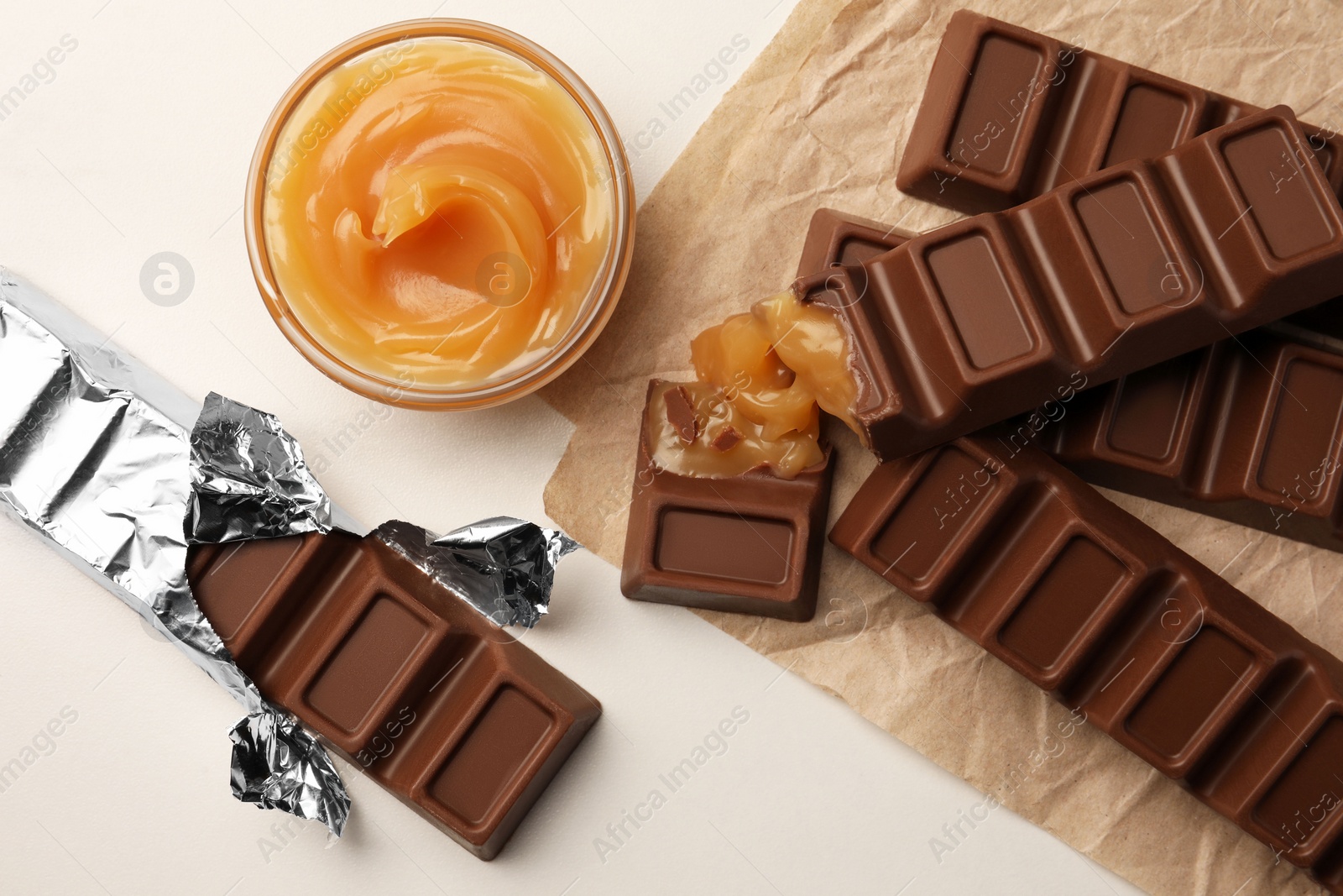 Photo of Tasty chocolate bars and bowl of caramel on white table, flat lay