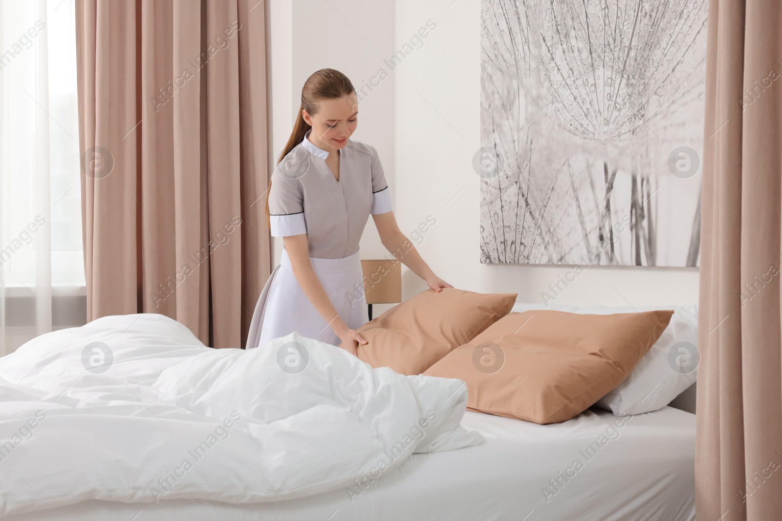 Photo of Young maid making bed in hotel room