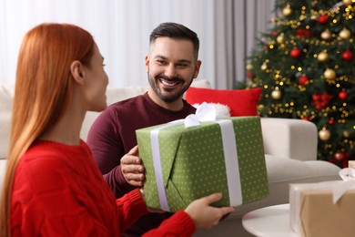 Photo of Christmas celebration. Woman and man exchanging gifts at home