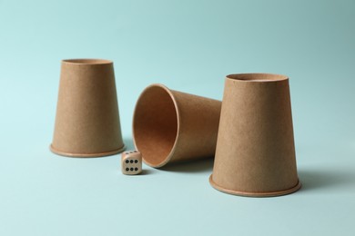 Photo of Three paper cups and dice on light blue background. Thimblerig game