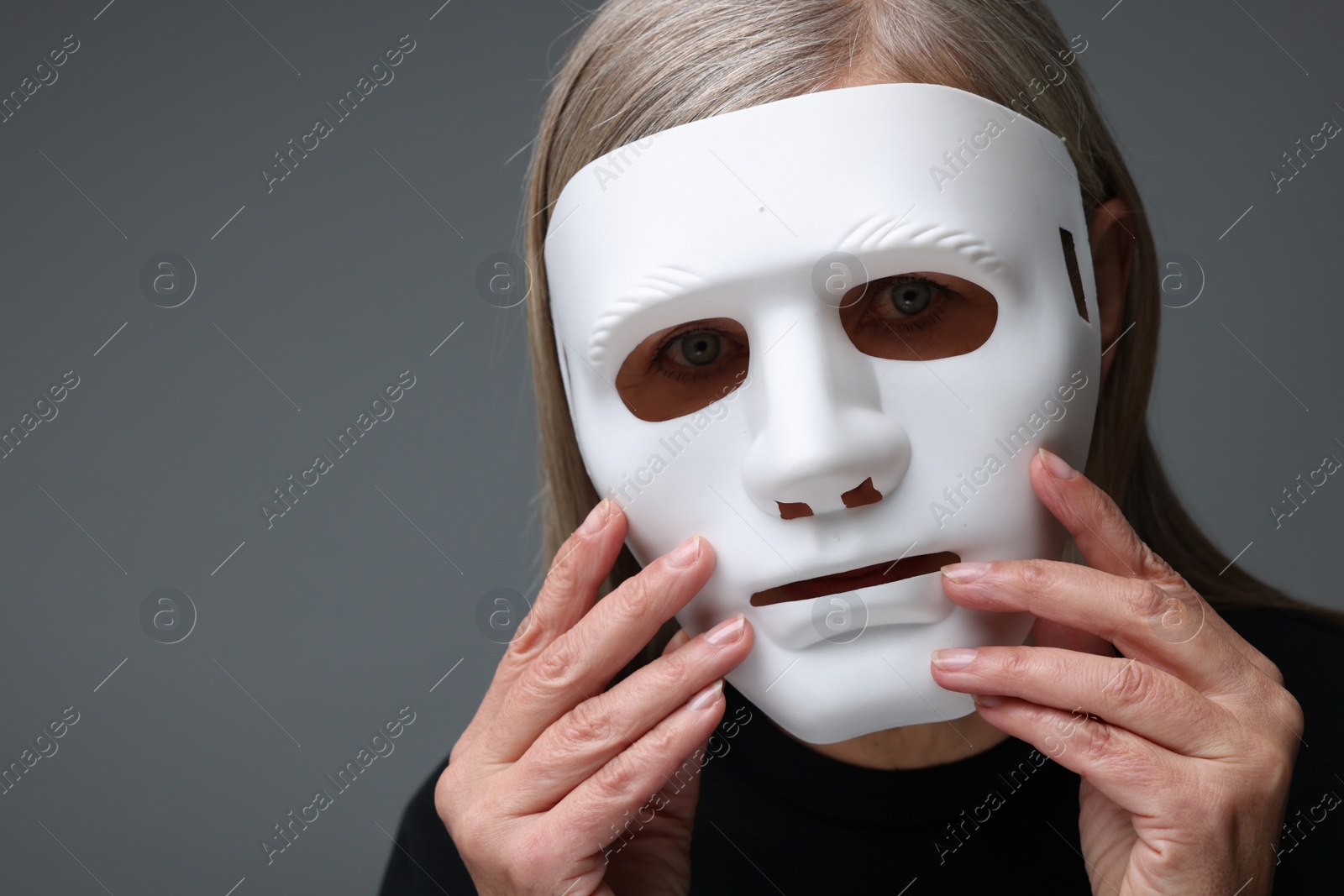 Photo of Multiple personality concept. Woman in mask on gray background, space for text