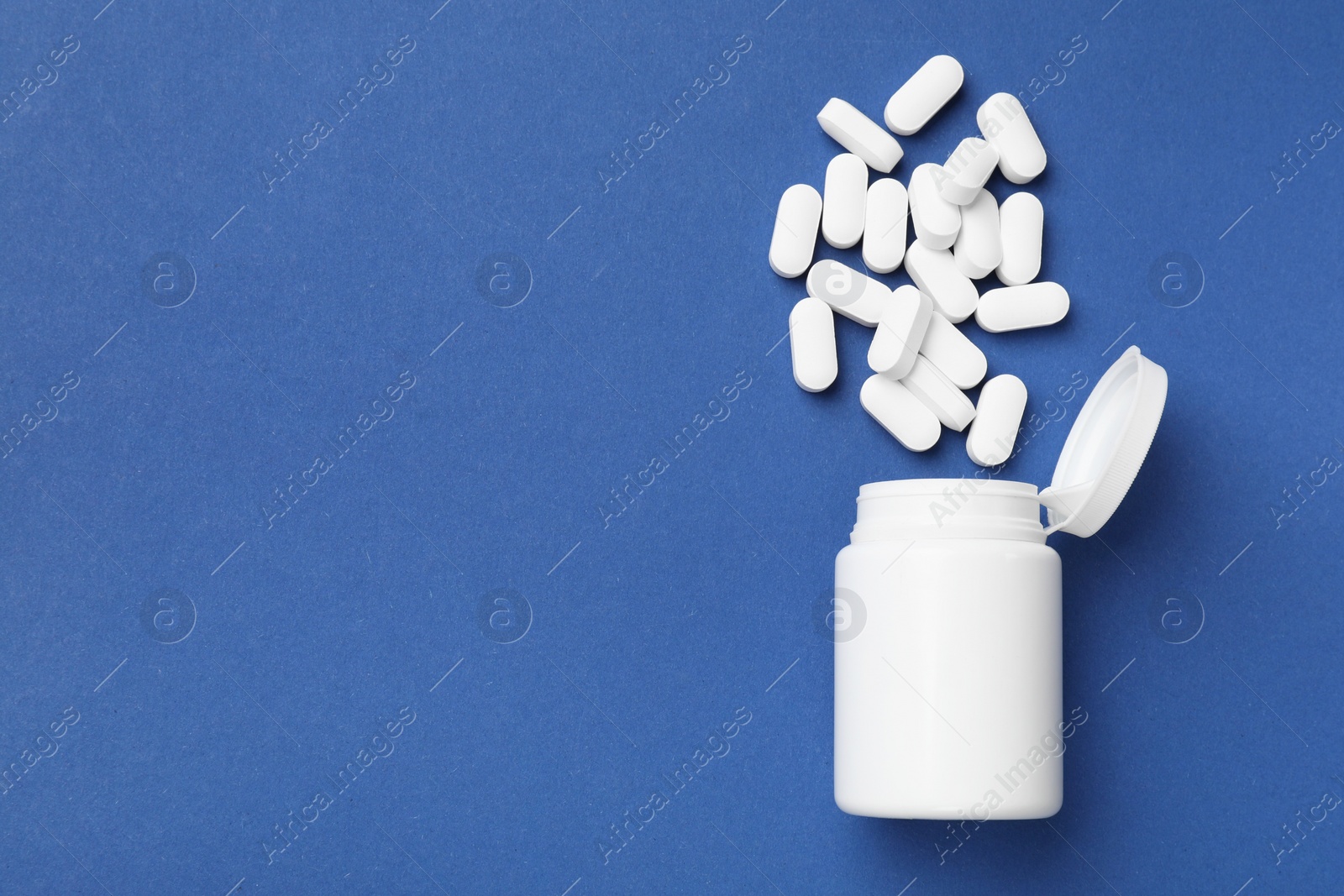 Photo of Vitamin pills and bottle on blue background, top view. Space for text