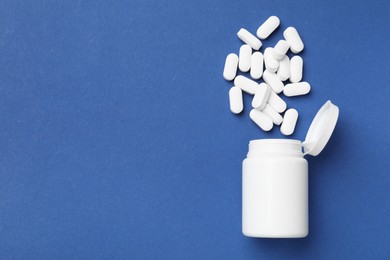 Vitamin pills and bottle on blue background, top view. Space for text