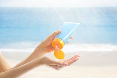 Young woman applying sun protection cream near sea, closeup