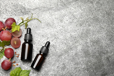 Bottles of natural grape seed oil on grey table, flat lay with space for text. Organic cosmetic