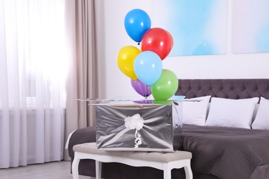 Photo of Gift box with bright air balloons in modern bedroom