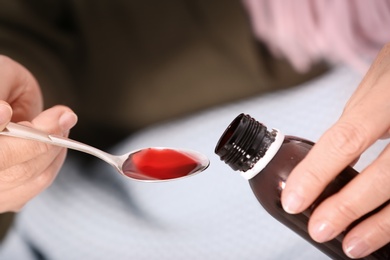 Photo of Ill mature woman with scarf taking cough syrup, closeup