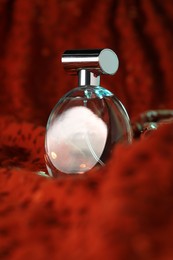 Photo of Luxury perfume in bottle on red fabric with sequins