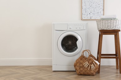 Photo of Laundry room interior with modern washing machine and wooden stool near white wall. Space for text