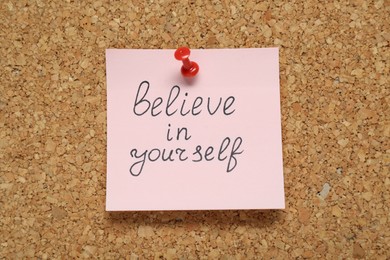 Photo of Note with phrase Believe In Yourself pinned on corkboard. Motivational quote