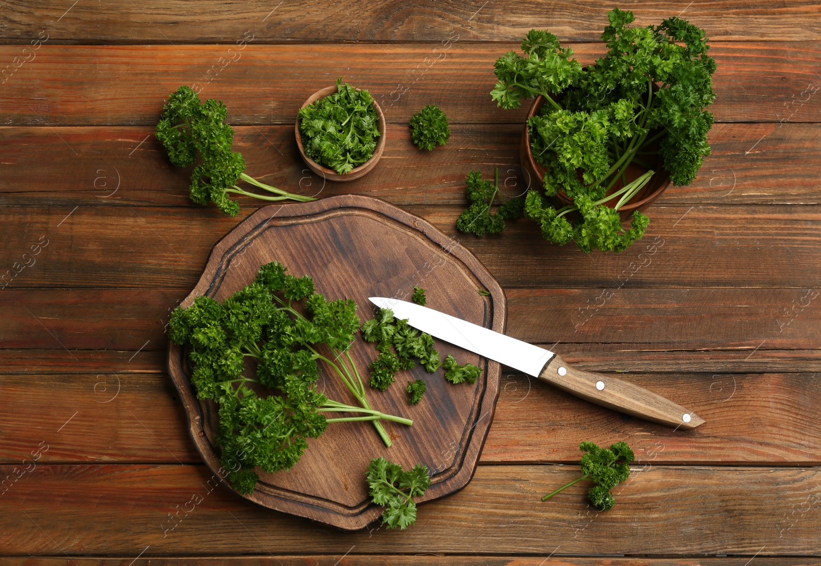 Photo of Fresh curly parsley, cutting board and knife on wooden table, flat lay