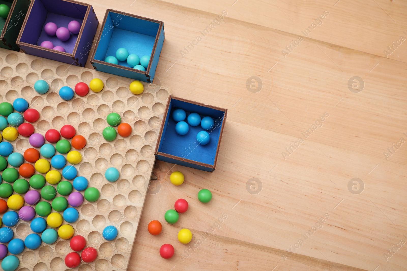 Photo of Wooden sorting board and boxes with colorful balls on table, flat lay. Montessori toy