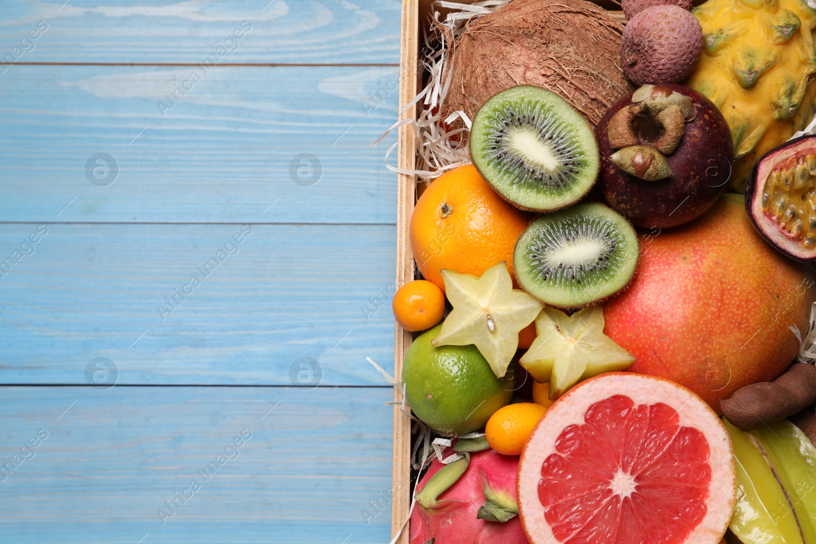 Photo of Different tropical fruits in box on blue wooden background, top view. Space for text