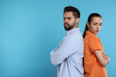 Resentful couple with crossed arms on light blue background, space for text