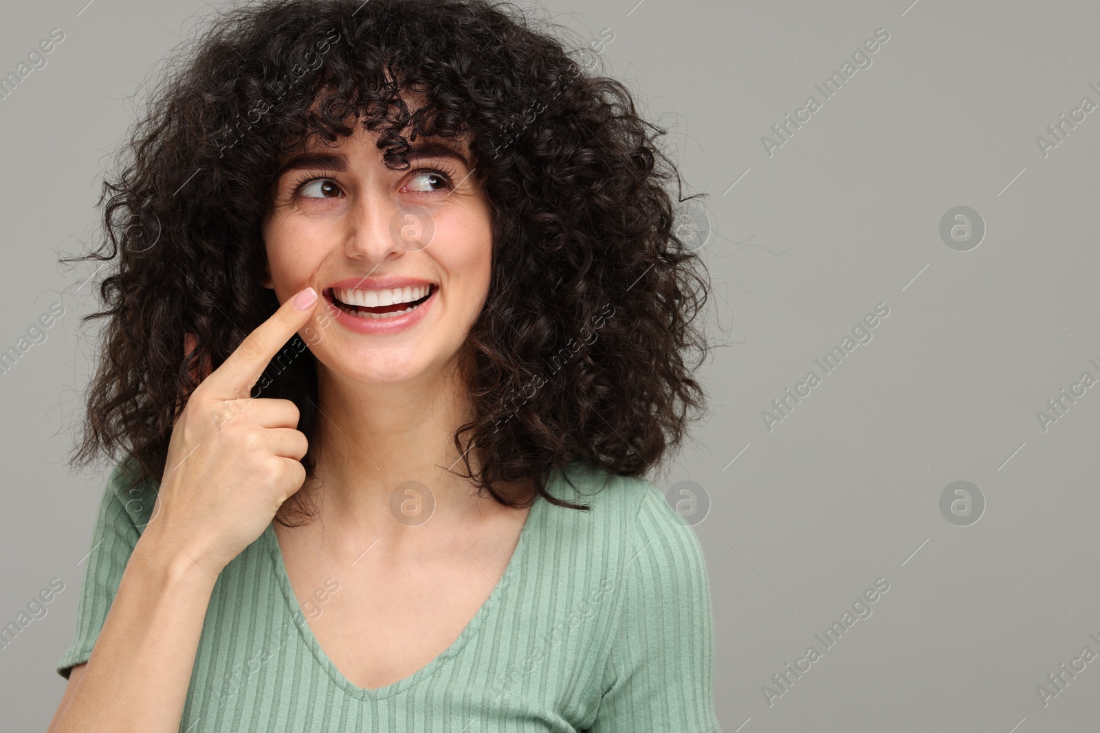 Photo of Young woman showing her teeth with whitening strip on grey background, space for text