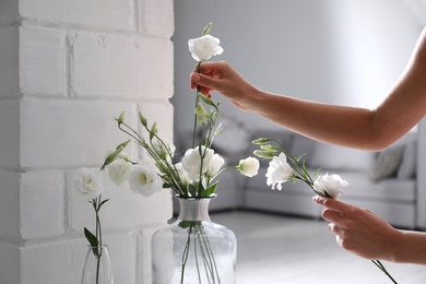 Photo of Woman taking beautiful flowers from vase indoors, closeup