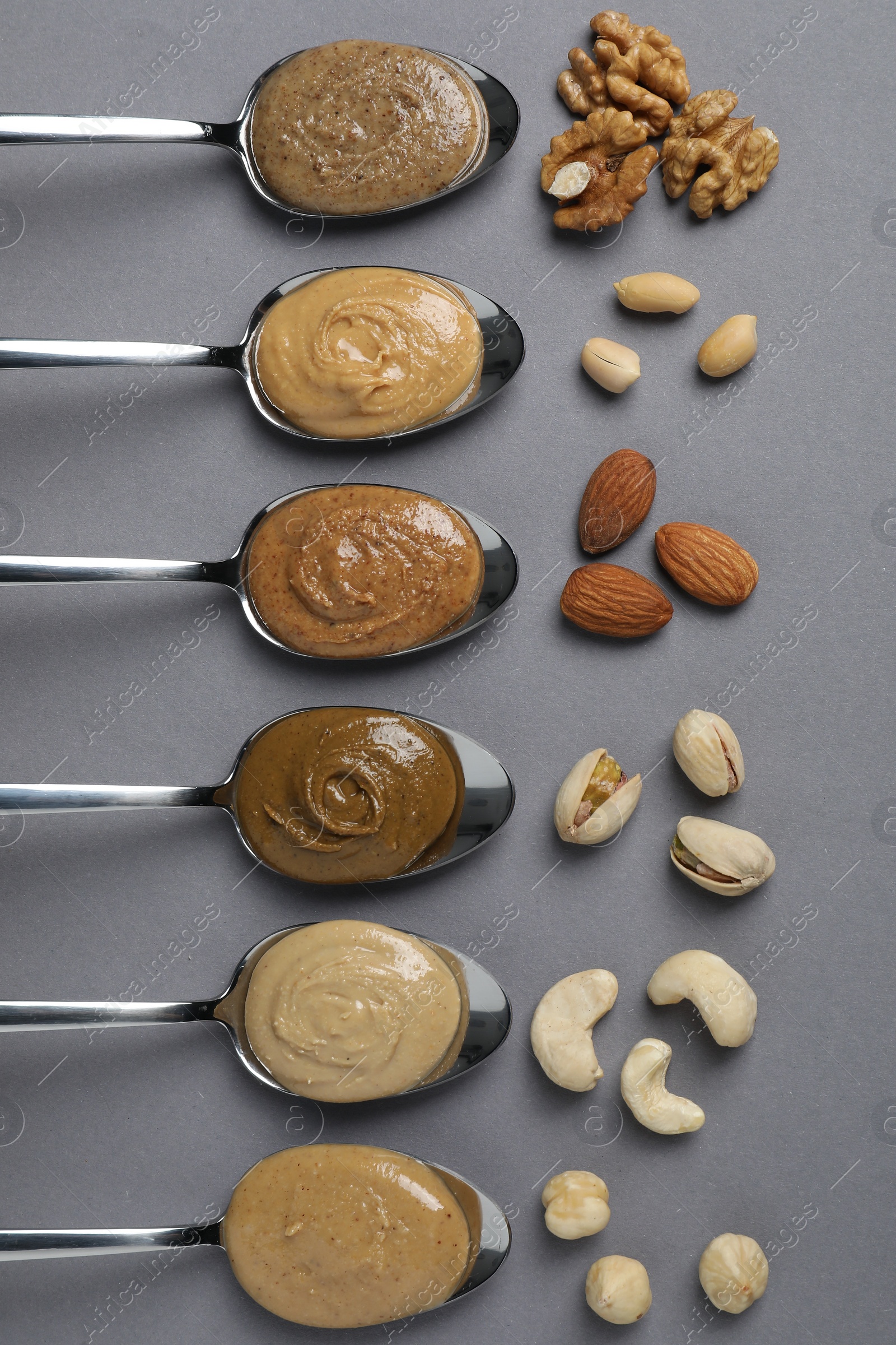 Photo of Tasty nut butters in spoons and raw nuts on gray table, flat lay