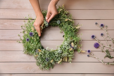 Woman making beautiful wreath of wildflowers at wooden table, top view