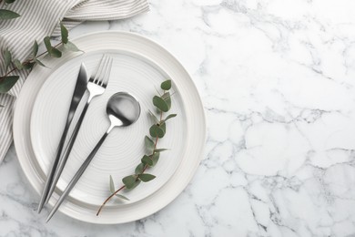 Stylish setting with cutlery, napkin, eucalyptus branches and plates on white marble table, top view. Space for text