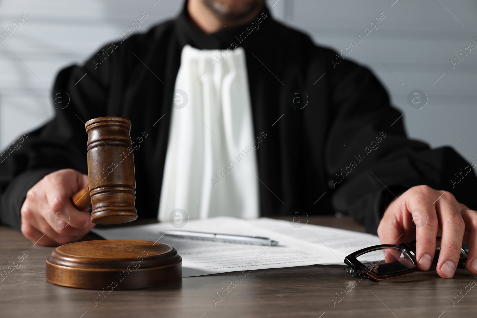 Photo of Judge with gavel, papers and glasses sitting at wooden table indoors, closeup