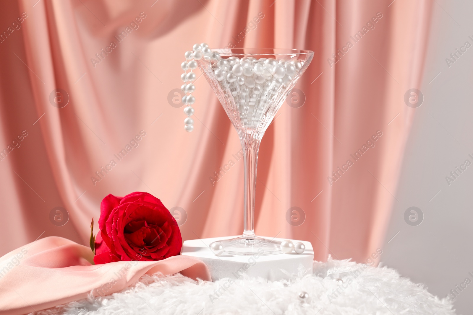 Photo of Martini glass with pearl beads and red rose on pink cloth