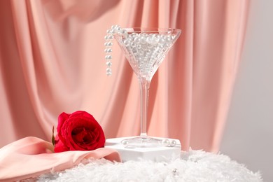 Photo of Martini glass with pearl beads and red rose on pink cloth