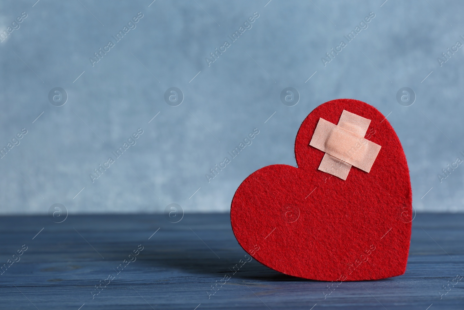 Photo of Red felt heart with adhesive plasters on table. Space for text
