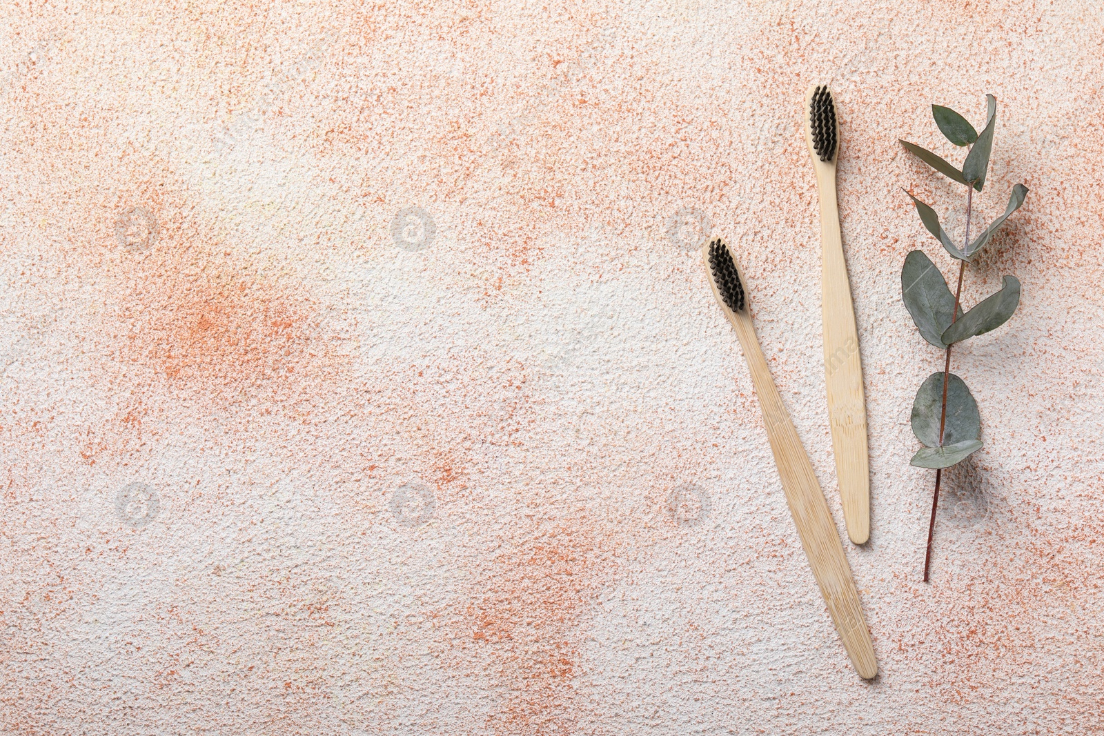 Photo of Bamboo toothbrushes and eucalyptus leaves on beige textured table, flat lay. Space for text