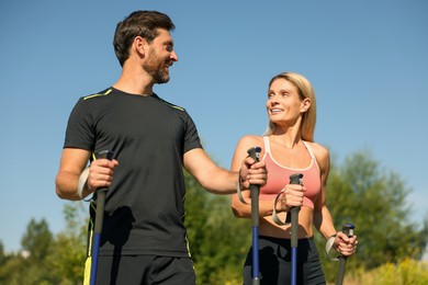 Happy couple practicing Nordic walking with poles outdoors on sunny day