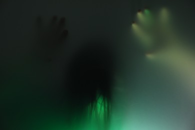 Photo of Silhouette of creepy ghost behind glass against color background