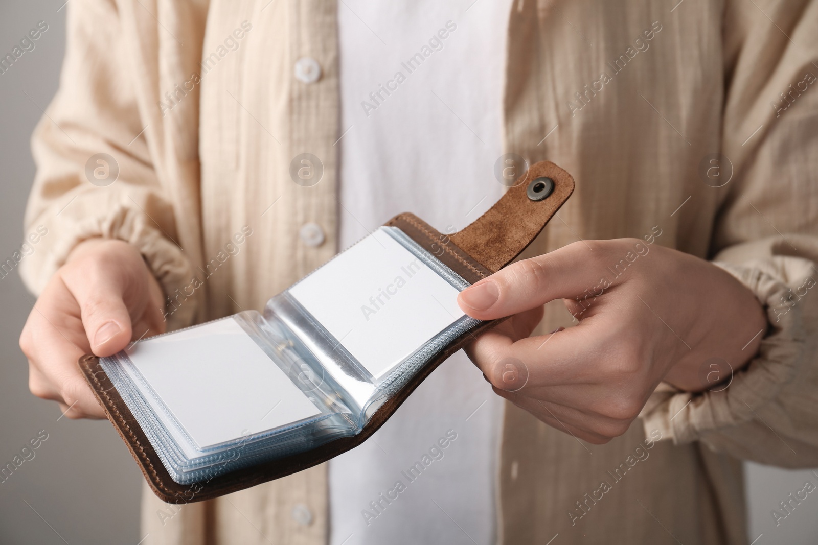 Photo of Woman holding leather business card holder with blank cards on grey background, closeup