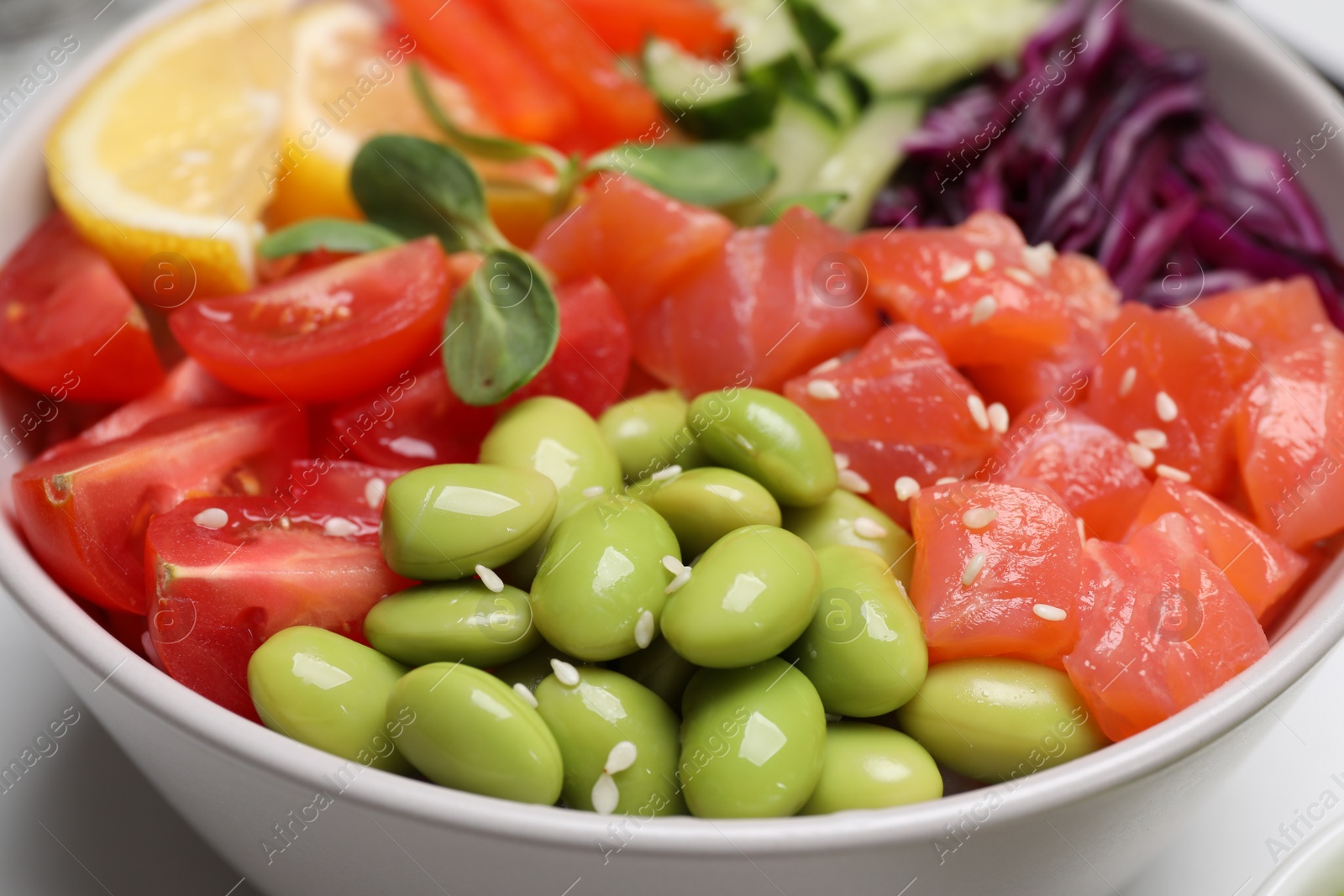 Photo of Poke bowl with salmon, edamame beans and vegetables on white table, closeup