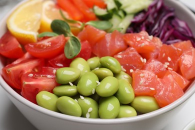 Poke bowl with salmon, edamame beans and vegetables on white table, closeup