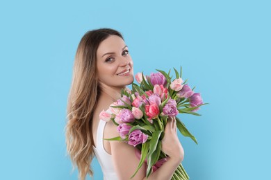 Happy young woman with bouquet of beautiful tulips on light blue background