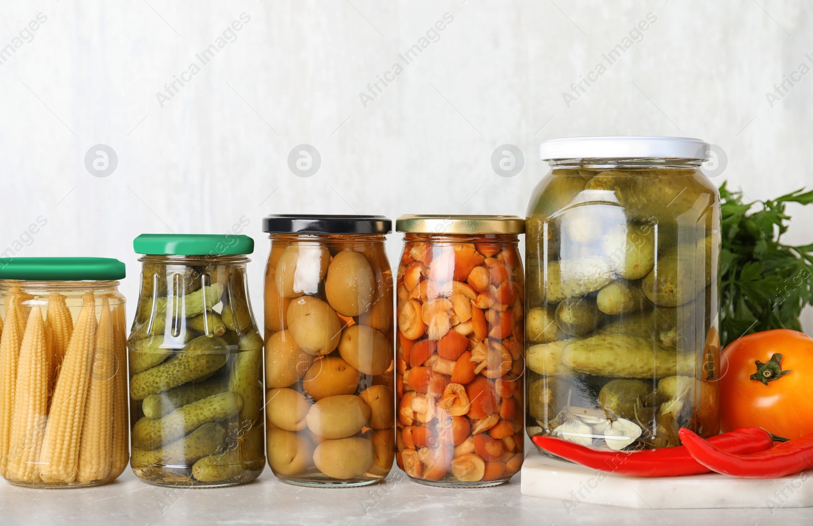 Photo of Glass jars with different pickled vegetables on light marble table