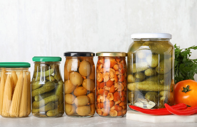 Glass jars with different pickled vegetables on light marble table