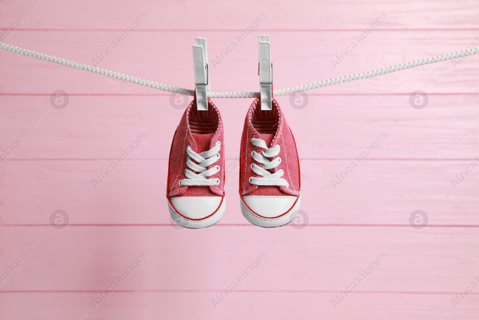 Photo of Cute baby sneakers drying on washing line against pink wooden wall