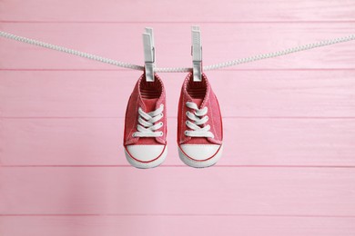Cute baby sneakers drying on washing line against pink wooden wall
