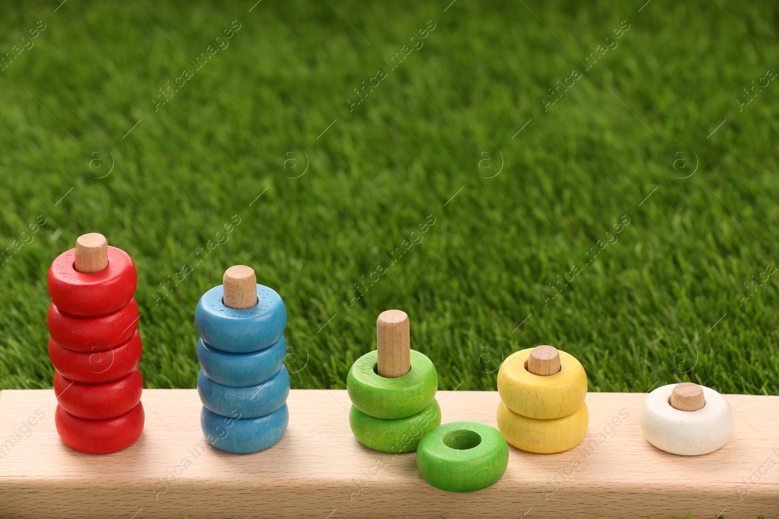 Photo of Stacking and counting game wooden pieces on artificial grass, space for text. Educational toy for motor skills development