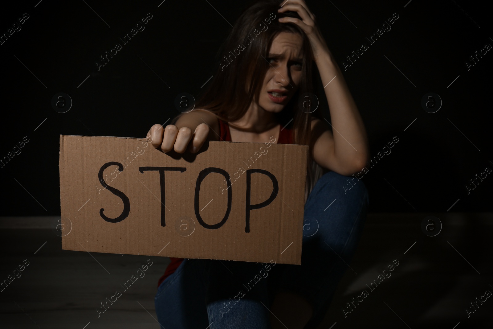 Photo of Crying young woman with sign STOP on black background. Domestic violence concept