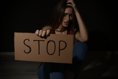 Crying young woman with sign STOP on black background. Domestic violence concept