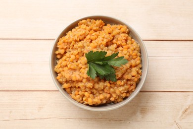 Photo of Delicious red lentils with parsley in bowl on wooden table, top view