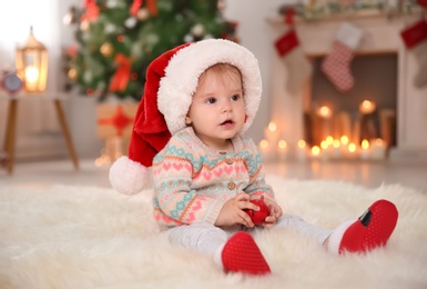 Cute little baby in Santa hat sitting on fur rug at home. Christmas celebration