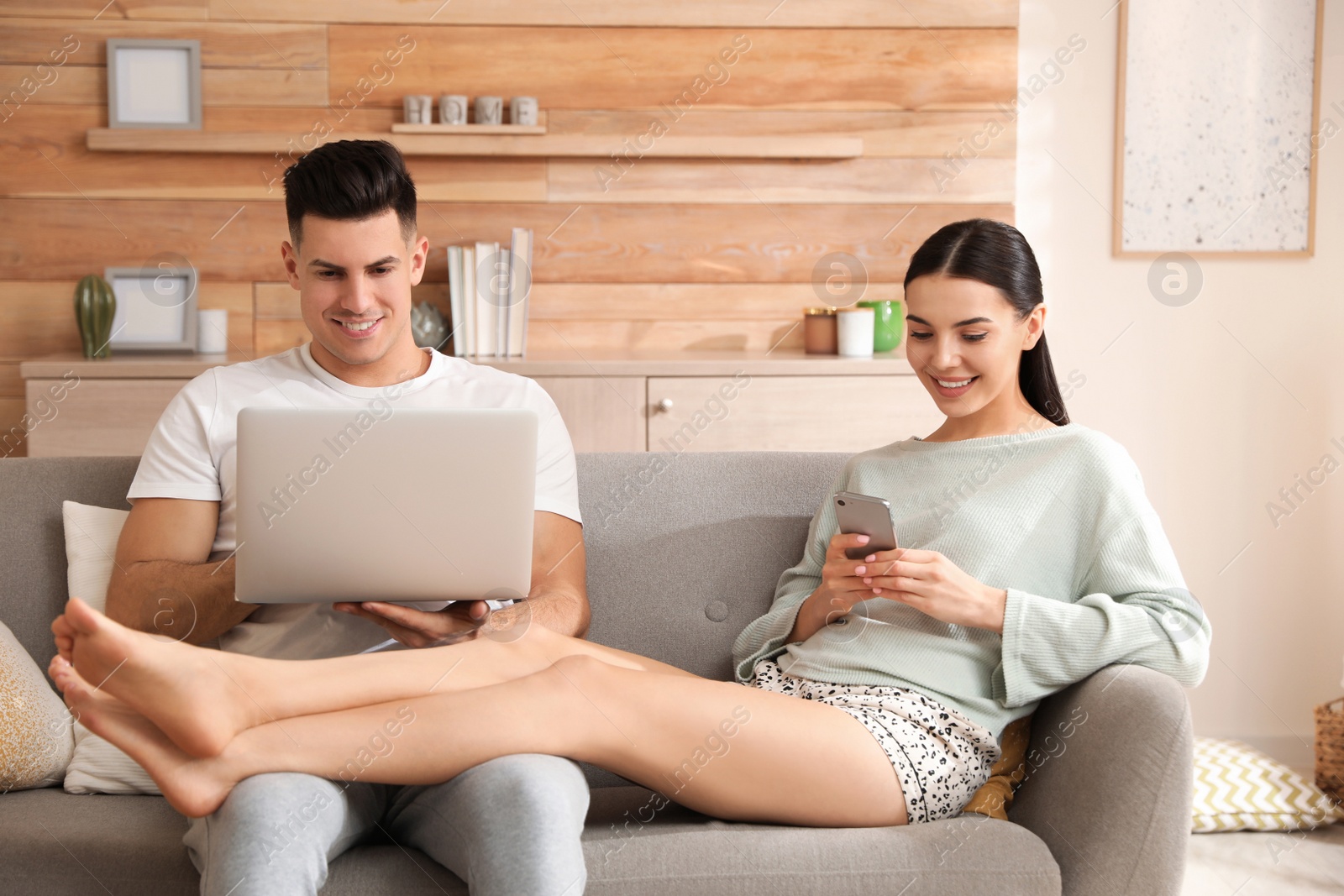 Photo of Happy couple in pyjamas with gadgets spending time together on sofa at home