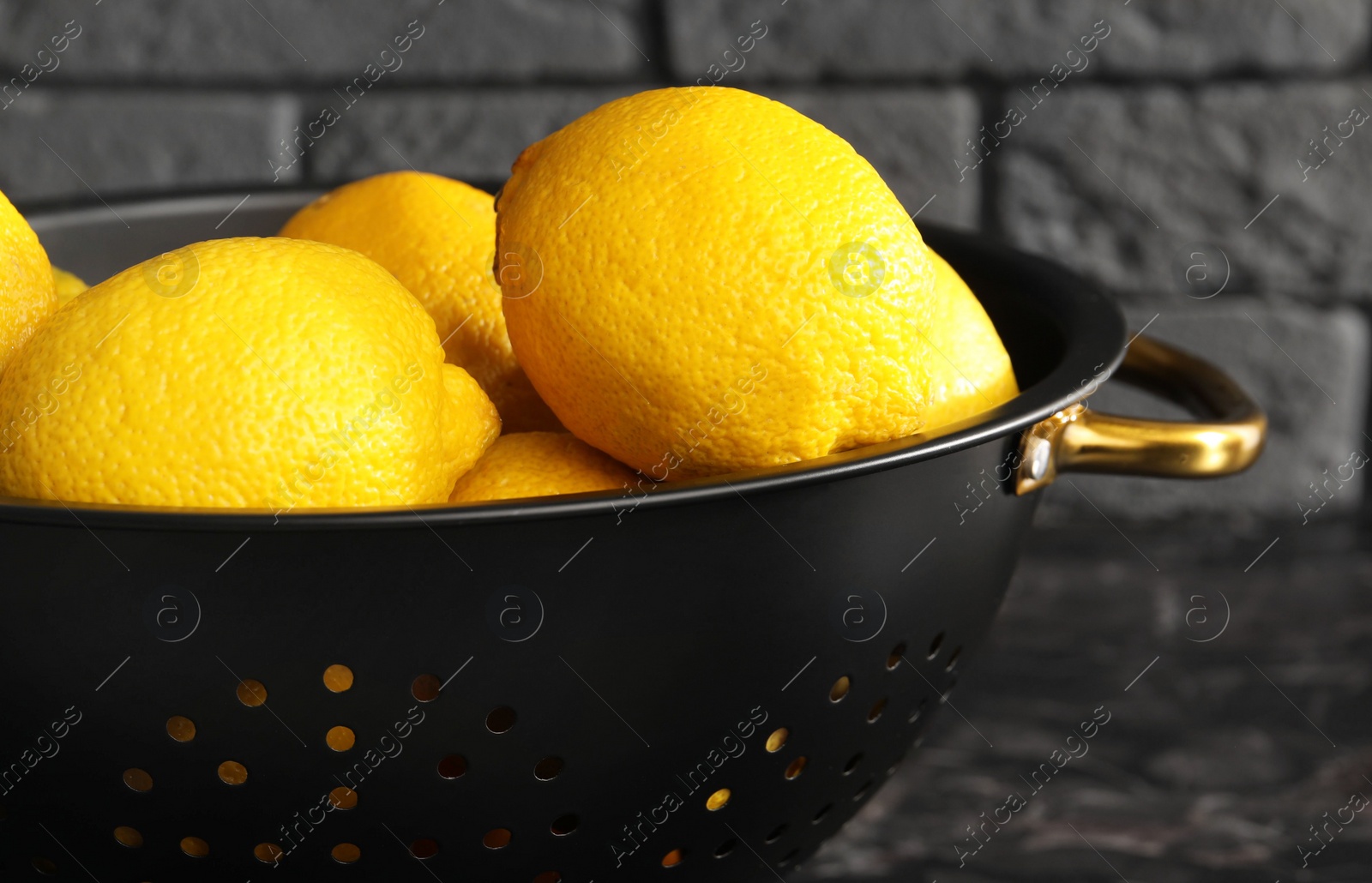 Photo of One colander with fresh lemons on black table, closeup