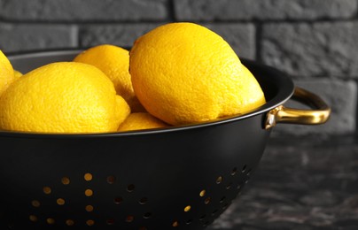 Photo of One colander with fresh lemons on black table, closeup